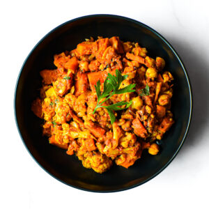 The Redneck Riviera: A black bowl filled with colorful vegetable curry, garnished with parsley, sits on a white surface.