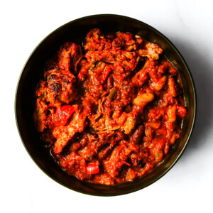 A bowl of The Redneck Riviera, a chunky stew with beans, tomatoes, and meat in a rich red sauce.