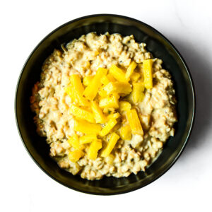 The Redneck Riviera: Creamy oatmeal in a black bowl, topped with chopped pineapple, viewed from above on a white surface.
