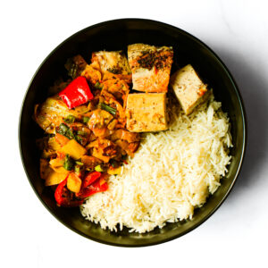 The Redneck Riviera: a black bowl filled with white rice, sautéed mixed veggies including bell peppers, and seasoned tofu pieces.
