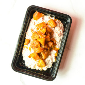 A black plastic tray of Adam & Eve Oats topped with cooked, seasoned apple chunks on a white surface.