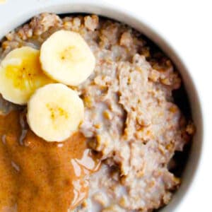 A bowl of oatmeal topped with banana slices and a generous drizzle of almond butter. The oatmeal has a creamy texture and fills most of the bowl, creating a warm and inviting breakfast display.