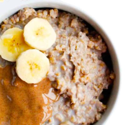 A bowl of oatmeal topped with banana slices and a generous drizzle of almond butter. The oatmeal has a creamy texture and fills most of the bowl, creating a warm and inviting breakfast display.