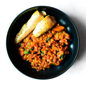 A bowl of Mac To The Face, a spiced lentil stew with vegetables, served with two pieces of roasted plantain.