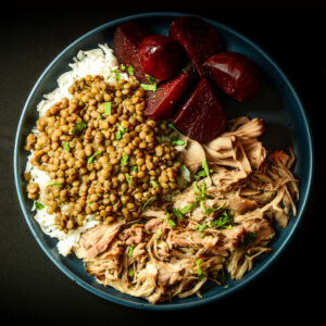 A blue plate with white rice, cooked lentils, shredded Oink & Destroy, and sliced beets, garnished with herbs.