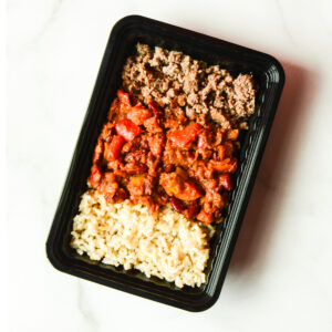 A black tray of Cluck The Bean offers ground beef, tomato-based vegetable stew, and cooked brown rice on a white surface.