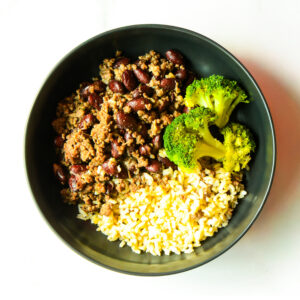 Cluck The Bean features ground beef, kidney beans, steamed broccoli florets, and cooked brown rice served in separate sections.