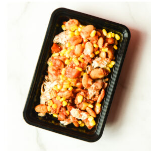 A black plastic tray of Cluck The Bean, featuring beans, corn, tomatoes, and meat pieces, is shown on a white surface.