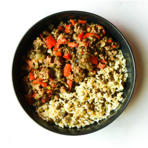 Cluck The Bean: A black bowl with cooked rice and lentils on one side, ground beef, red bell peppers, and onions on the other.