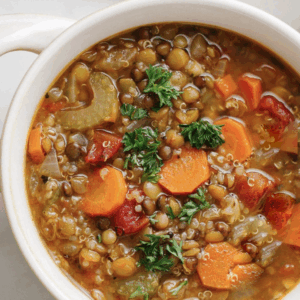 A bowl of Smokey Mountain Stew with sliced carrots, tomatoes, lentils, and parsley garnish in a white soup bowl.