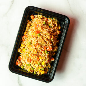 A black plastic container of Mean Mexi-Machine mixed fried rice with corn, peas, carrots, and other veggies on a light marble surface.