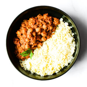 Operation Cajun Fit: A black bowl with white rice and chickpea curry, garnished with parsley, viewed from above.