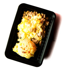 A black plastic tray contains Operation Cajun Fit: a serving of cheesy ground meat casserole and baked bread or biscuit.