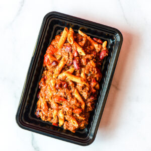 Mean Mexi-Machine: Black plastic container with cooked penne, ground meat, red kidney beans, and tomato sauce on white marble.