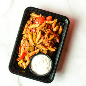 The Mean Mexi-Machine: Penne pasta with ground meat and bell peppers in a black container, served alongside white sauce.