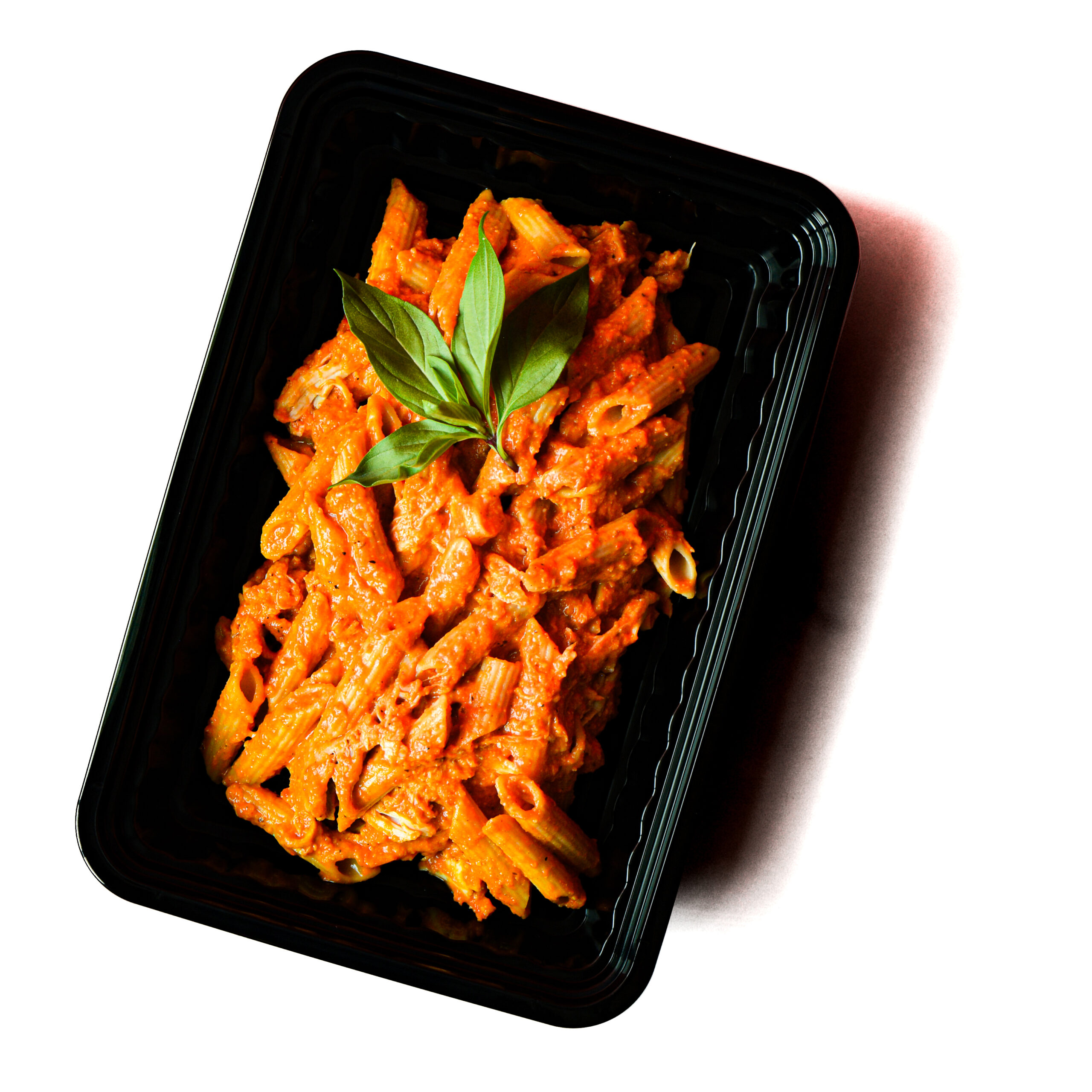 Operation Cajun Fit in a black plastic container with penne pasta in red sauce, garnished with basil, on a white background.