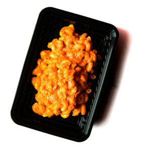 A black plastic container of Operation Cajun Fit creamy orange macaroni and cheese, shown on a white background.