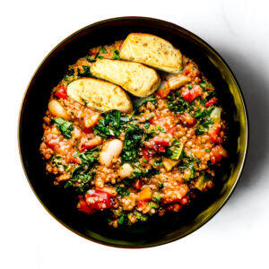 Engine 38 Tortellini features a bowl of tortellini pasta with quinoa, white beans, greens, tomatoes, and three roasted potato wedges on a white background.