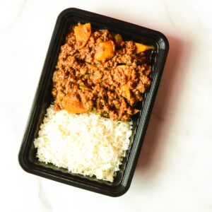 A black plastic container of Southwest Shenanigans, You Clucker! holds white rice and a ground meat stew with potatoes on a white surface.
