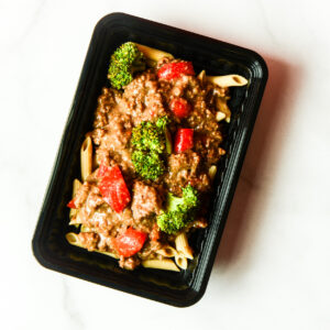 Southwest Shenanigans, You Clucker! in a black plastic container with penne, ground beef sauce, broccoli, and red bell pepper on a white surface.