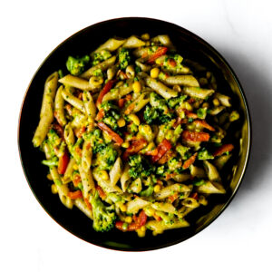 A bowl of Engine 38 Tortellini mixed with broccoli, corn, and red bell peppers in a light sauce on a white background.