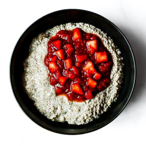 A bowl of Engine 38 Tortellini sits on a white surface, topped with chunky strawberry sauce.