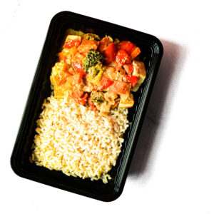 A black meal tray containing cooked brown rice and a serving of Chickpeas & Beef? Savvy! with broccoli, red bell peppers, and sauce.