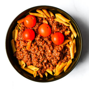 A black bowl of Engine 38 Tortellini topped with meat sauce and cherry tomatoes, viewed from above on a white background.