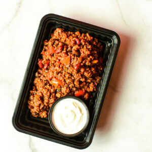Flexican Fiesta: Black plastic tray with chili (ground meat, beans, tomatoes) and a side of white sour cream.