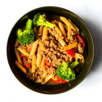 A bowl of Engine 38 Tortellini with ground meat, broccoli florets, and red bell peppers on a white background.