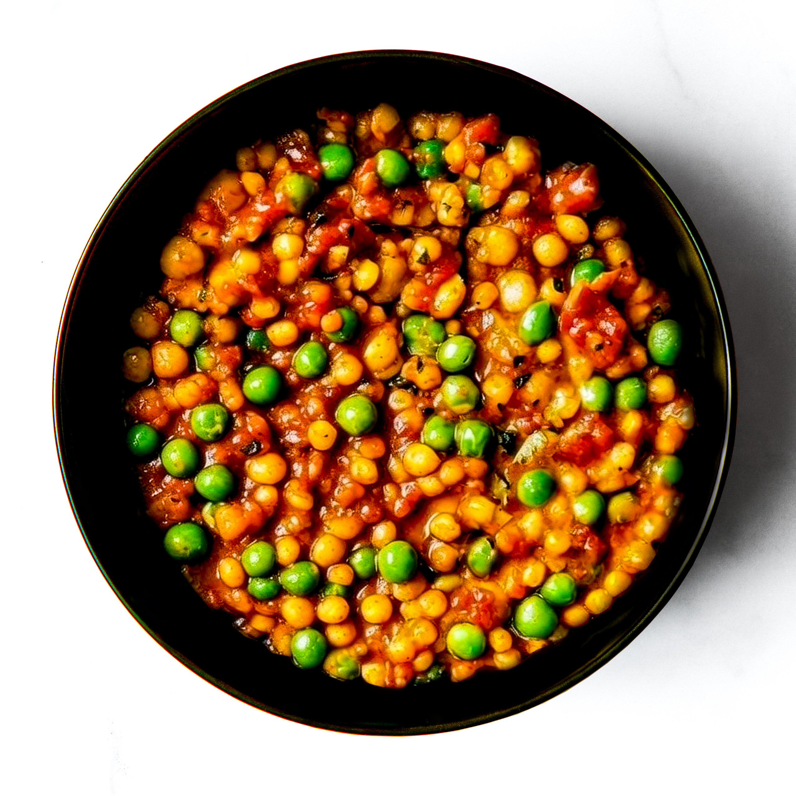 A black bowl of Engine 38 Tortellini, a tomato-based stew with yellow lentils and green peas, seen from above on a white background.