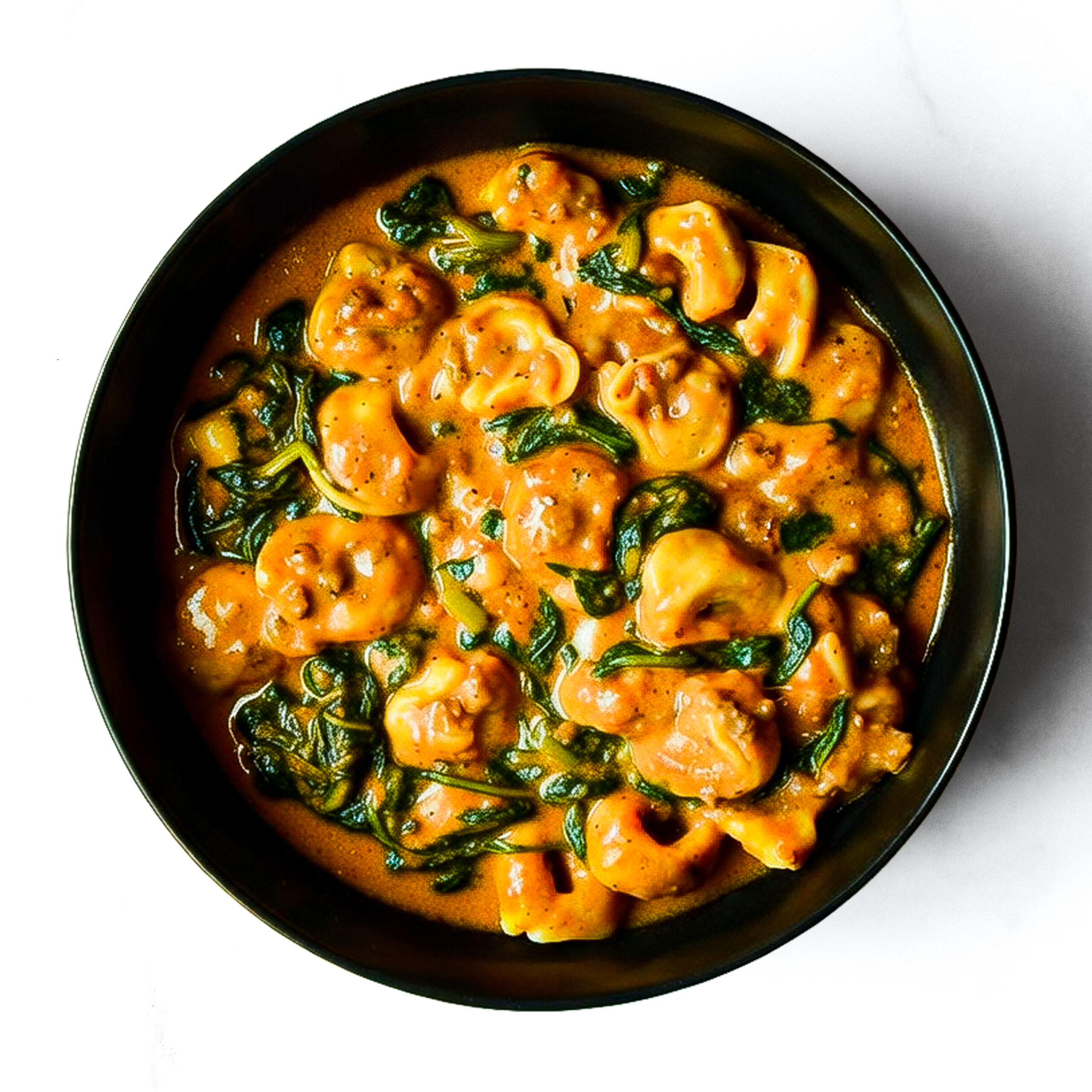 Engine 38 Tortellini in a creamy orange sauce with spinach, served in a black bowl and viewed from above on a white surface.