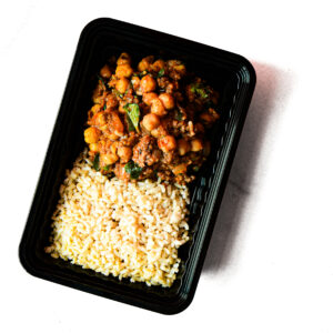A black meal prep container of Chickpeas & Beef? Savvy! with brown rice on one side and stew on the other, set against a white background.