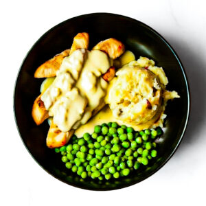 A black plate featuring Engine 38 Tortellini topped with creamy sauce, served with mashed potatoes and green peas.