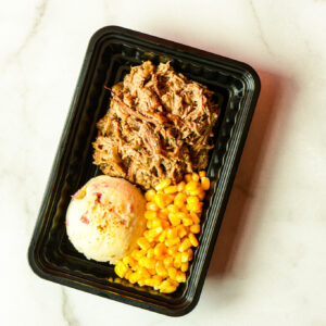 The Flexican Fiesta features shredded beef, mashed potatoes, and corn served in a black meal tray on a light-colored surface.