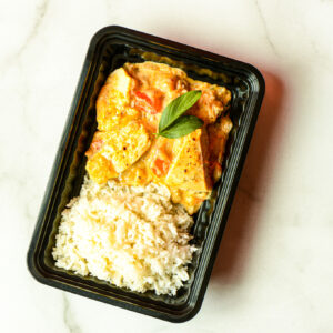 The Flexican Fiesta is a black plastic food container with white rice and curry with tofu, topped with basil, shown on a white surface.