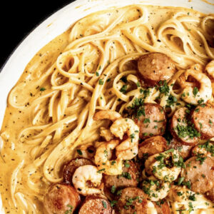Pasta Voodoo: Creamy pasta with cooked shrimp and sliced sausage, topped with chopped herbs, served in a white pan.