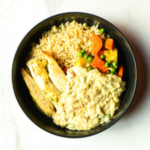 Pardon My French… Clucker: a bowl with brown rice, grilled chicken breast, peas, carrots, corn, and creamy beige sauce on the side.