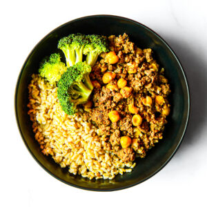 A black bowl featuring Alfredo del Bombero with brown rice, steamed broccoli, and ground meat with chickpeas.
