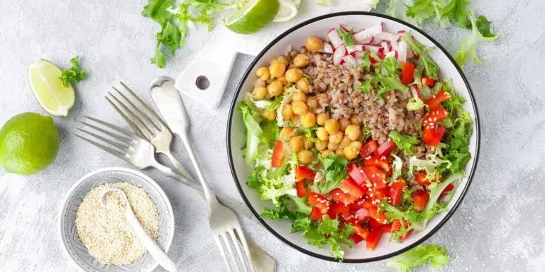 A bowl filled with lettuce, chickpeas, buckwheat, diced red bell pepper, sliced radish, and sesame seeds—perfect for a plant-based meal delivery experience.