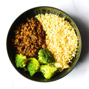 A bowl of BeefZilla ground meat, yellow rice, and steamed broccoli on a white surface.