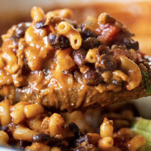 A close-up of a spoonful of Cheesus Mac & Cheese with macaroni, black beans, ground meat, and tomato sauce.