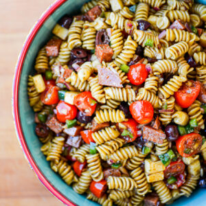 A bowl of The Angry Korean pasta salad with cherry tomatoes, black olives, cubed cheese, green peppers, salami, and vinaigrette.