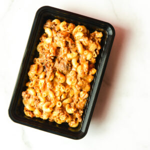 Black plastic container filled with baked macaroni and cheese with ground beef, placed on a white marble surface.