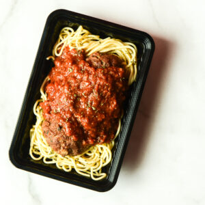 A black plastic container holding cooked spaghetti topped with meatballs and marinara sauce, placed on a white surface.