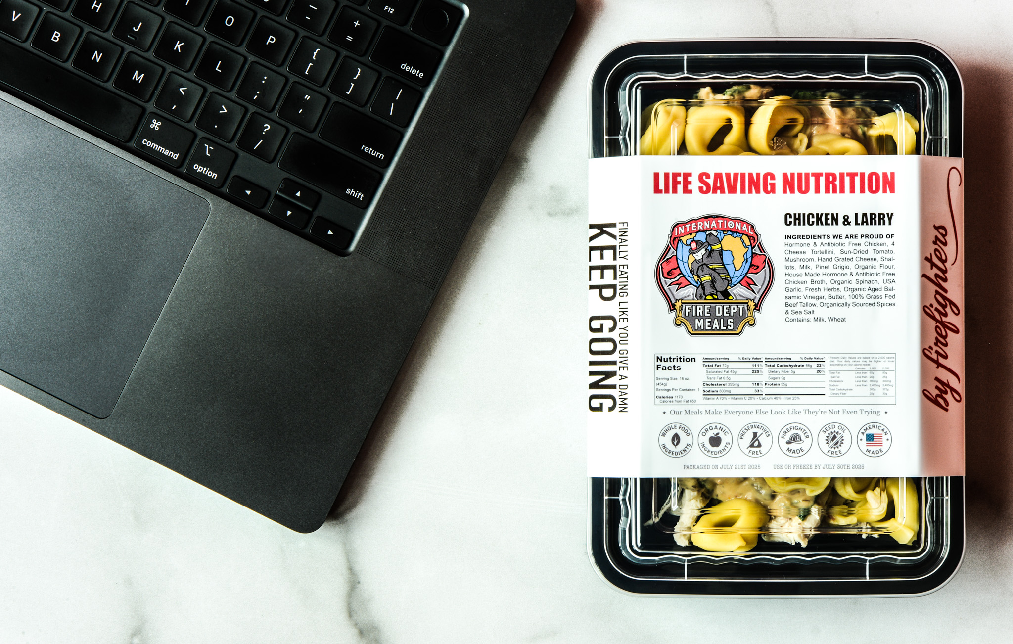 A packaged meal labeled Life Saving Nutrition: Chicken & Larry sits beside a laptop on a white surface. The meals nutrition label and branding are visible.