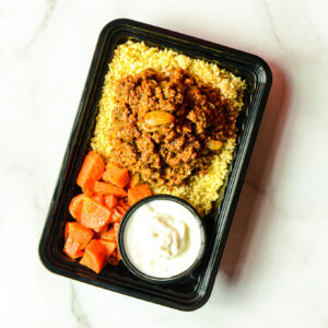 The Angry Korean: Black plastic meal container with ground meat on couscous, cooked carrots, and white sauce in a small cup.