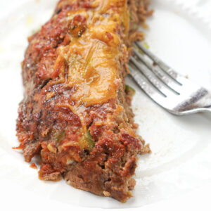 Pa! The Meatloaf, served on a white plate with melted cheese and tomato sauce, comes with a fork.