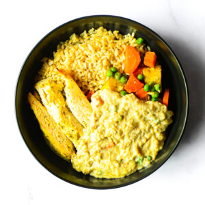 Jack'd-Atouille: A bowl with yellow rice, grilled chicken breast slices, peas and carrots, and creamy yellow sauce.