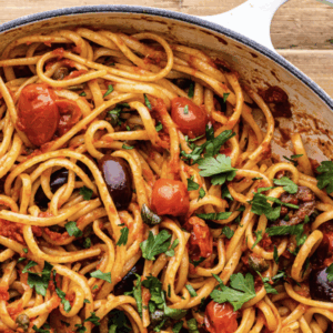 Cooked spaghetti mixed with Don’t Call Me Marinara sauce, cherry tomatoes, black olives, capers, and fresh parsley in a large pan.